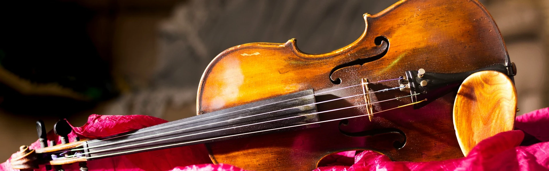 A violin lies on its right side on rumpled pink cloth.