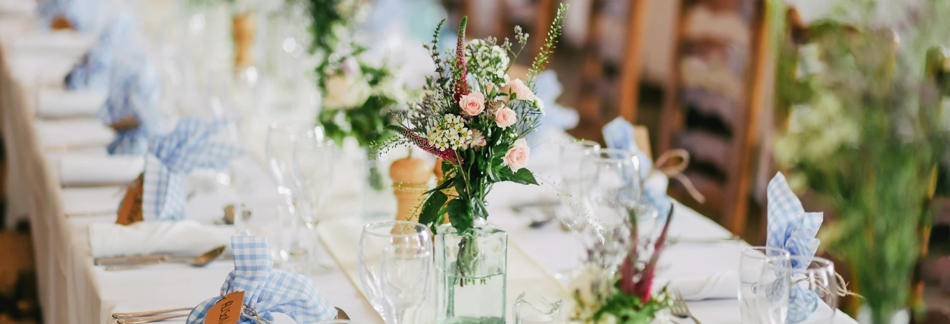 A bouquet sits on a table with with white tablecloth and decorative table-settings.