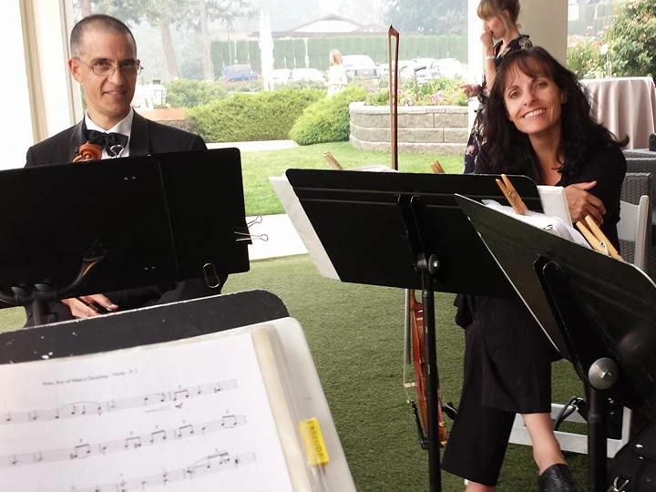 Two smiling violinists sitting behind music stands.