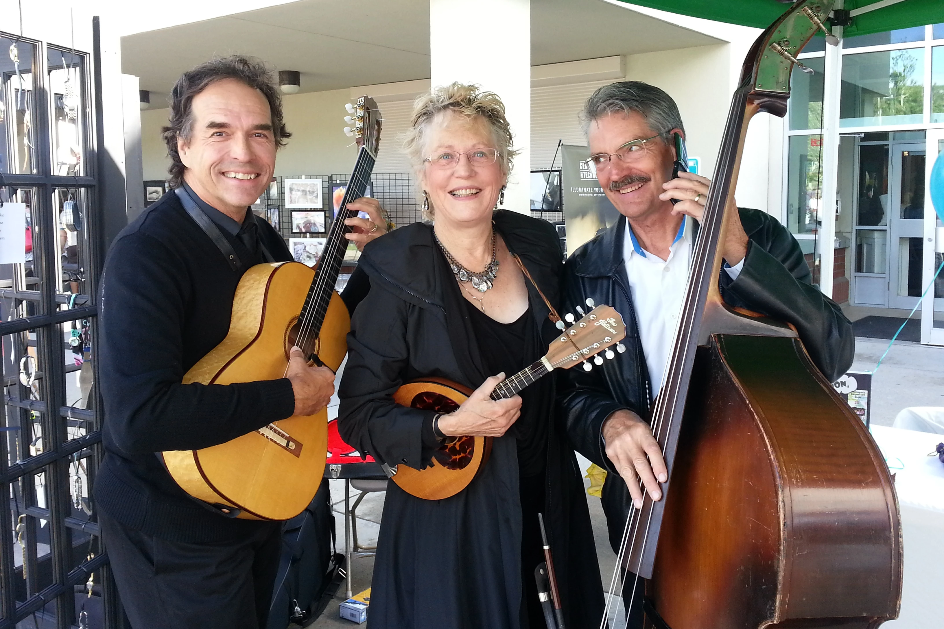 A guitarist, mandolin player, and bassist pose for the camera. The bassist is comedically pretending to talk to someone on a folding cell-phone.