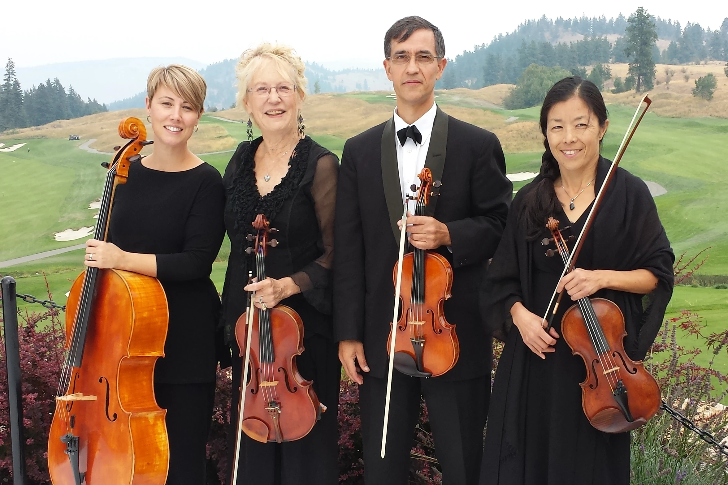 A string quartet poses in front of the grassy hill of a golf course.