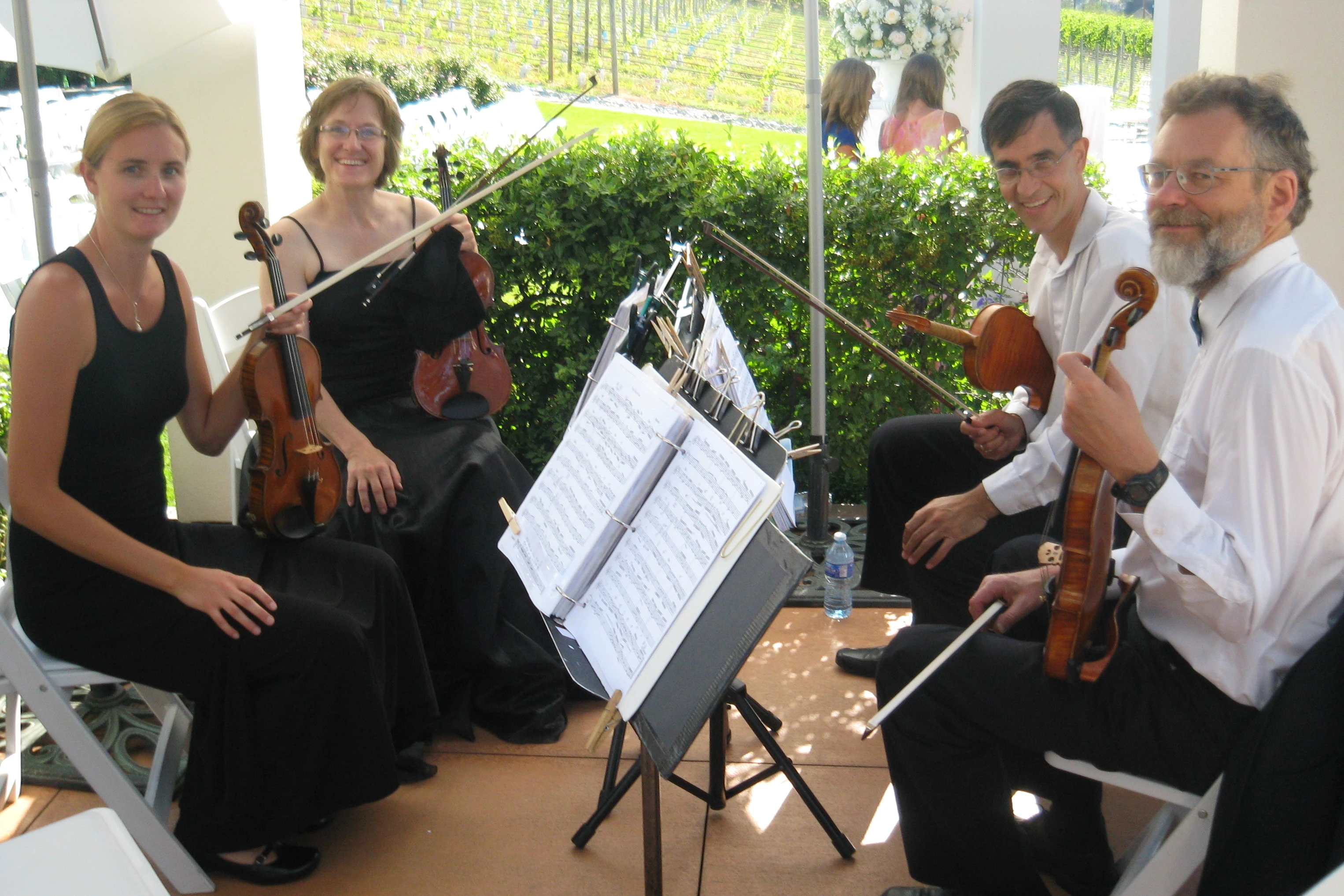 String quartet members in black and white formalwear sit on either side of some music stands, smiling at camera.