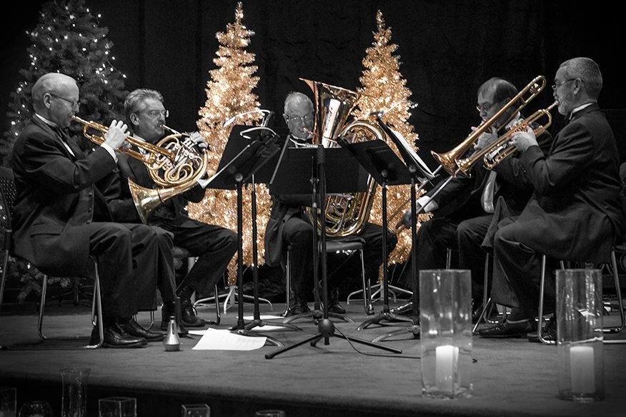 A brass quintet plays in front of two golden Christmas trees.