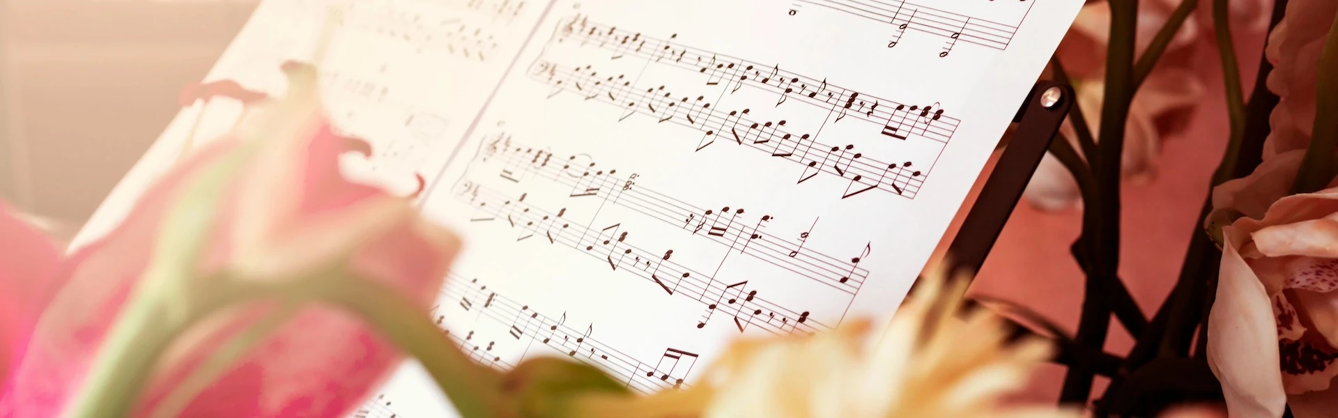 Sheet-music on a music stand, seen from the right side. Blurry flowers obscure the foreground.