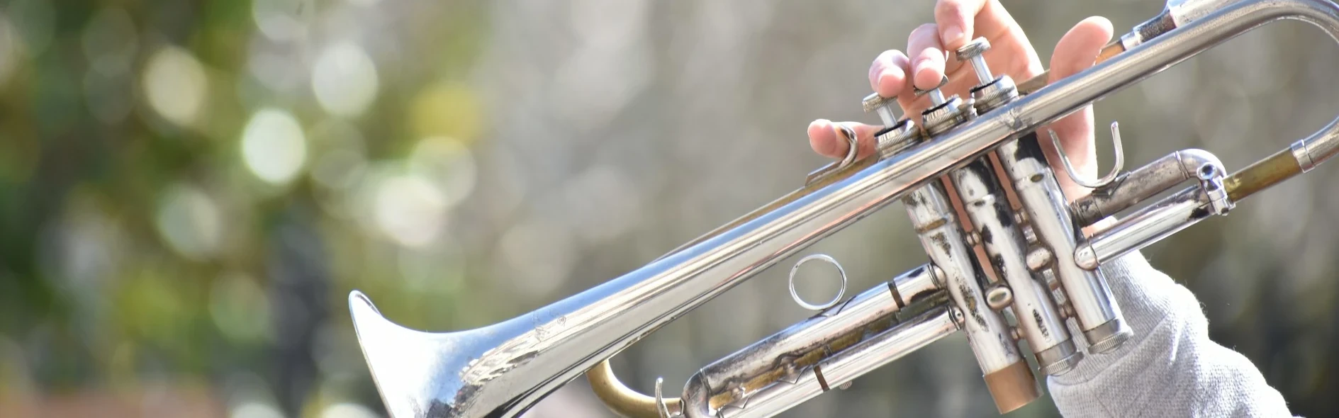 A silver trumpet being held by the hand of a musician outside of frame to the right.